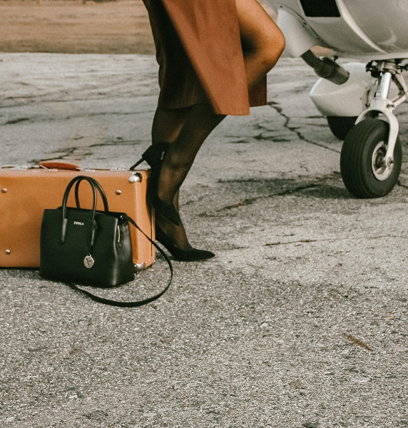 Stylish traveler with luggage beside a private jet on an empty runway, symbolizing luxury air travel.
